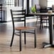 A black ladder back chair with an antique walnut wood seat.