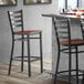 A Lancaster Table & Seating black ladder back bar stool with a wooden seat.