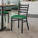 A Lancaster Table & Seating black ladder back chair with a green vinyl padded seat at a table in a restaurant.