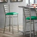 A Lancaster Table & Seating Ladder Back Bar Stool with a green vinyl padded seat.