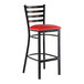 A metal bar stool with a ladder back design and a red vinyl padded seat.