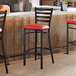 A ladder back bar stool with a distressed copper finish and a red vinyl padded seat.