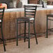 A black metal ladder back bar stool with a dark brown vinyl padded seat.