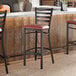 A black ladder back bar stool with a burgundy vinyl padded seat.