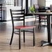 A black ladder back chair with a mahogany wood seat in a restaurant setting.