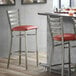 A Lancaster Table & Seating ladder back bar stool with a burgundy vinyl padded seat next to a bar counter.