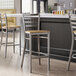 A Lancaster Table & Seating bar stool with a driftwood seat and clear coat finish on a chair next to a counter.