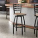 A black metal ladder back swivel bar stool with a driftwood-colored wooden seat.