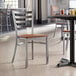 A Lancaster Table & Seating clear coat finish ladder back chair with an antique walnut wood seat at a table in a restaurant.