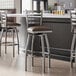 A group of Lancaster Table & Seating swivel bar stools with dark brown vinyl padded seats next to a counter.
