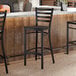 A black metal bar stool with a ladder back design and a black wood seat, placed at a counter.