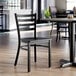 A black ladder back chair with a black wood seat, designed for dining or restaurant use.