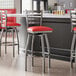 Lancaster Table & Seating Clear Coat Finish Ladder Back Swivel Bar Stool with red vinyl padded seats at a bar counter.