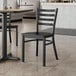 A Lancaster Table & Seating black metal ladder back chair with a black wood seat at a table in a restaurant.