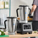 A heavy duty commercial food blender with a stainless steel base, variable speed controls, and two large stainless steel jars.