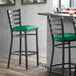 A Lancaster Table & Seating black ladder back bar stool with a green vinyl padded seat.