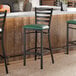 A black metal bar stool with a ladder back design and a green vinyl padded seat.
