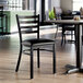 A black ladder back chair with a padded vinyl seat and a distressed copper finish, placed in a restaurant setting.