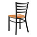 A Lancaster Table & Seating black metal ladder back chair with a cherry wood seat.