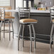 A group of Lancaster Table & Seating ladder back swivel bar stools with light brown vinyl padded seats next to a counter.