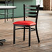 A Lancaster Table & Seating black ladder back chair with a red vinyl padded seat on a table in a restaurant dining area.