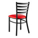 A Lancaster Table & Seating black metal ladder back chair with a red padded seat.