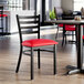 A black ladder back chair with a red vinyl padded seat.