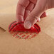 A hand using a red TamperSafe label to close a brown envelope.