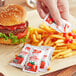 A person holding a French's tomato ketchup packet and putting it on a hamburger.