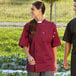 A woman wearing a Uncommon Chef burgundy short sleeve chef coat.