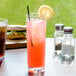 A Roc N' Roll SAN plastic Collins glass filled with pink liquid and a straw with a lemon slice.