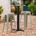 A black Lancaster Table & Seating table base with two stools on a brick patio.