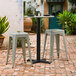 A Lancaster Table & Seating black outdoor table base with a black pole on a brick patio with a black plate and a black candle holder.