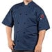 A man wearing a navy short sleeve Uncommon Chef coat with a customizable logo in a professional kitchen.