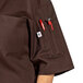 A man wearing a brown Uncommon Chef short sleeve chef coat with red pockets.