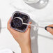 A hand using an OXO tea ball to scoop dried tea leaves from a container.