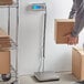 A person using the San Jamar Escali Granda receiving scale to weigh a box.