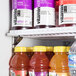 An Avantco black sliding glass door merchandiser refrigerator filled with bottles of liquid.