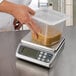 A chef weighing liquid in a plastic container on a San Jamar portion scale.