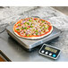 A pizza with toppings on a black San Jamar digital portion scale.