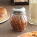 An American Metalcraft Lexan plastic spice shaker with red and yellow flakes on a table.