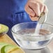 A person holding a spoon with Regal Citric Acid powder on it over a bowl of water.