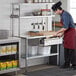 A man in a chef's uniform preparing food on a Regency stainless steel work table.