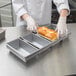 A person in a white coat holding a loaf of bread in a metal tray.