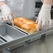 A person wearing white gloves putting a loaf of bread into a Chicago Metallic aluminized steel bread loaf pan.