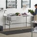 A man standing at a Regency stainless steel work table in a kitchen holding a bunch of vegetables.