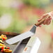 A hand holding a Dexter-Russell solid turner over a tray of food.