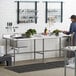 A man using a Regency stainless steel work table with a sink in a kitchen.