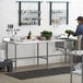 A woman standing at a Regency stainless steel work table with a sink.