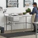 A woman in an apron uses a Regency Cross Brace on a work table in a kitchen.